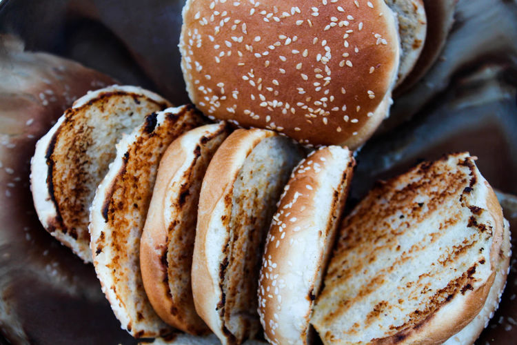 Grilled hamburger buns with sesame seeds in a metal bowl.
