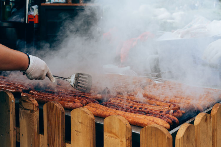Cropped image of hand cooking sausages on barbecue grill
