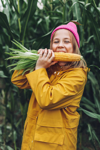 Funny little girl dressed in a yellow raincoat and a hot pink cap spoils and bites corn 