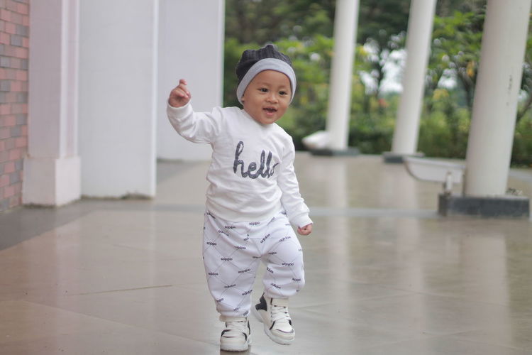 Cute and adorable toddler with a cute smile while standing on the floor in a sporty white costume