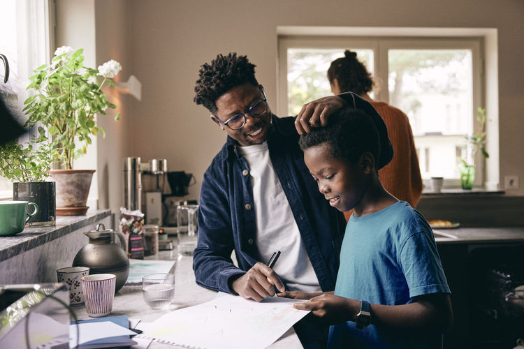 Smiling father caressing hair of son doing homework at home