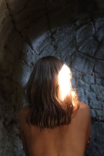 Rear view of shirtless woman standing against wall