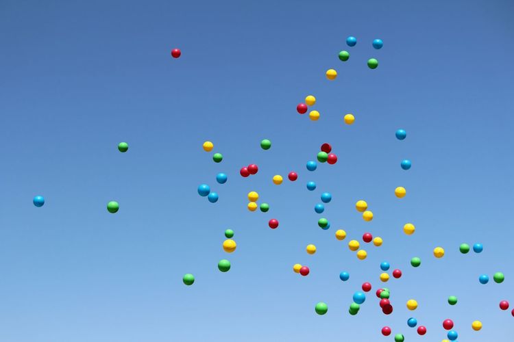 Low angle view of multicolor balloons flying against blue sky