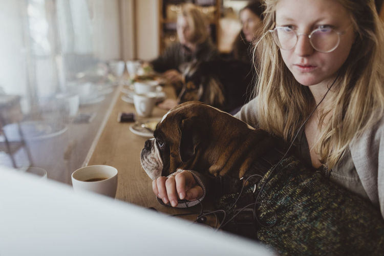 Young woman sitting with boxer dog while using laptop at cafe
