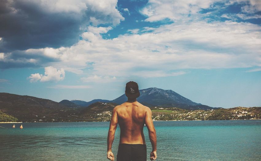 Rear view of shirtless muscular man standing by sea against sky