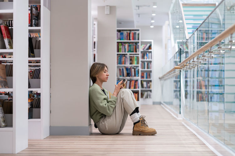 Full length of young woman using mobile phone in library