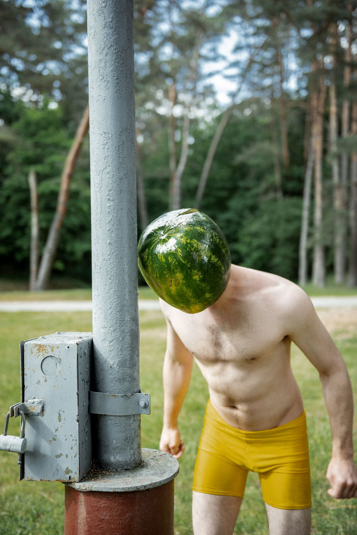 Shirtless man wearing face covered with watermelon on land