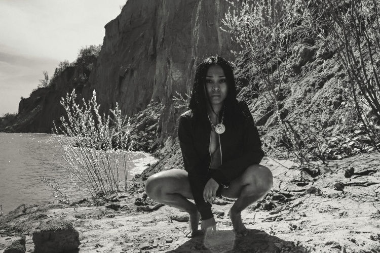 Portrait of seductive woman crouching by lake during sunny day