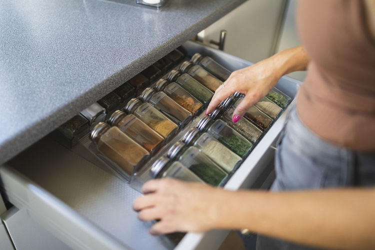 Hands of woman arranging spice jars in kitchen drawer