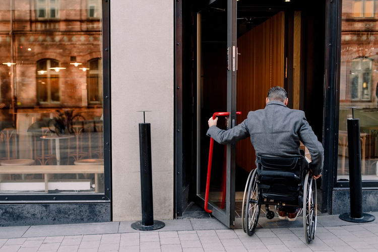 Rear view of disabled mature man sitting on wheelchair while entering in store