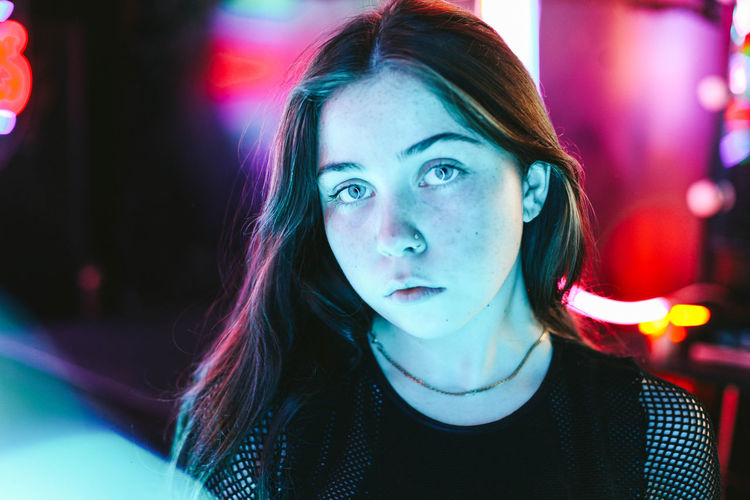 Close-up portrait of beautiful young woman against illuminated lights