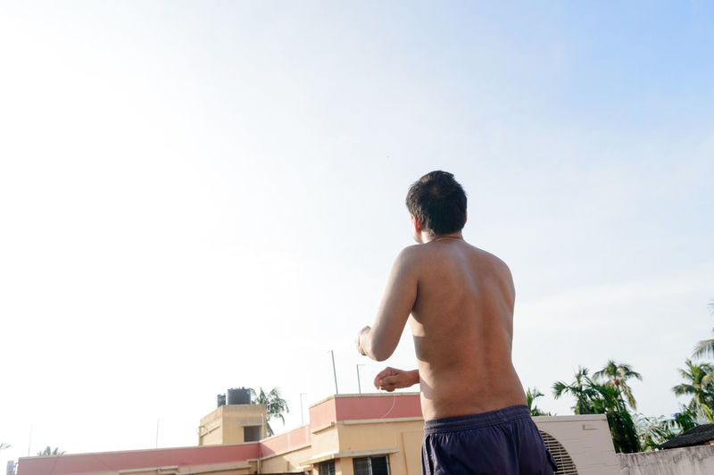 Rear view of shirtless man standing against sky