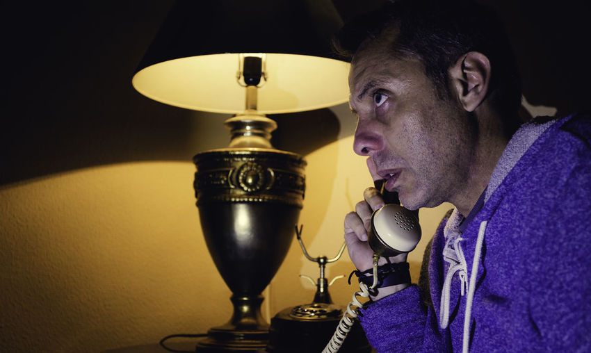 Man talking on telephone by electric lamp at home