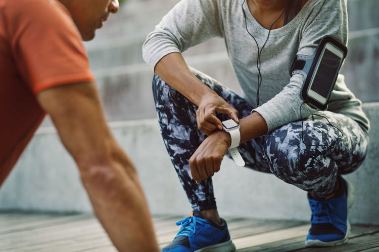 Woman using smart watch while friend doing push-ups on steps