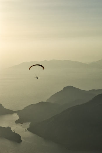 Silhouette person paragliding over lake against mountains during sunset