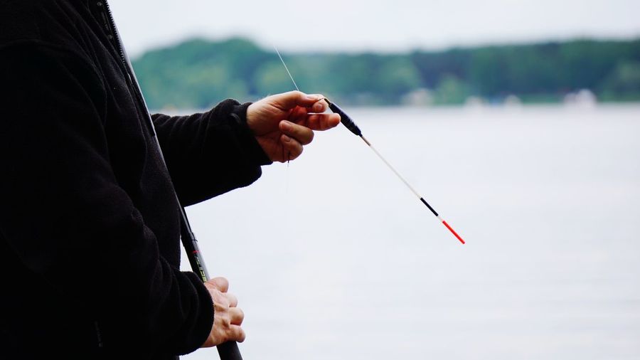 Midsection of man holding fishing rod against blurred background