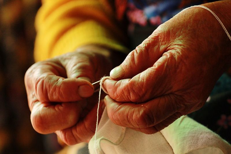 Cropped hands of woman stitching fabric at home