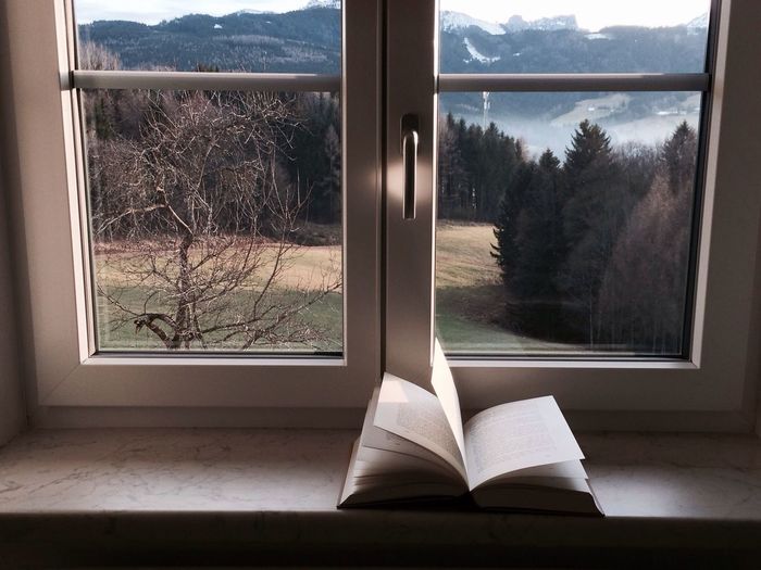 Book on window sill in front of scenic view of mountain through window