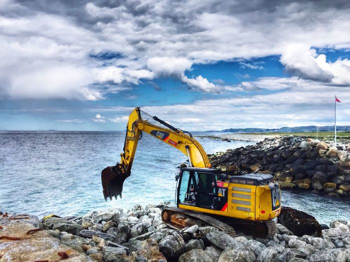 Earth mover on rocks by sea against cloudy sky