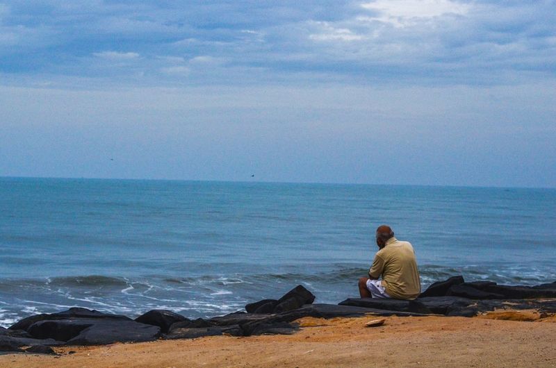 Man sitting on beach against sky