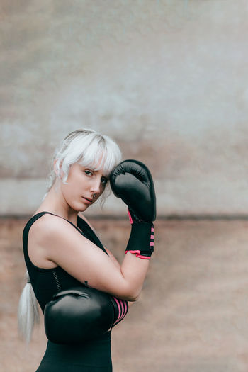 Portrait of woman with boxing gloves standing against wall
