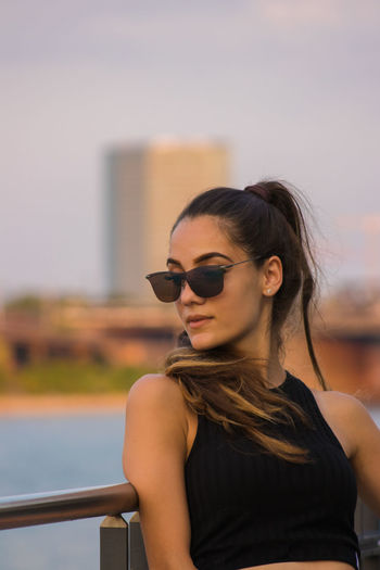 Young woman wearing sunglasses by railing against sky