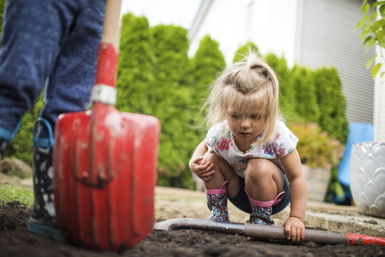 Cute young girl inspects dirt, looking for bugs and worms.