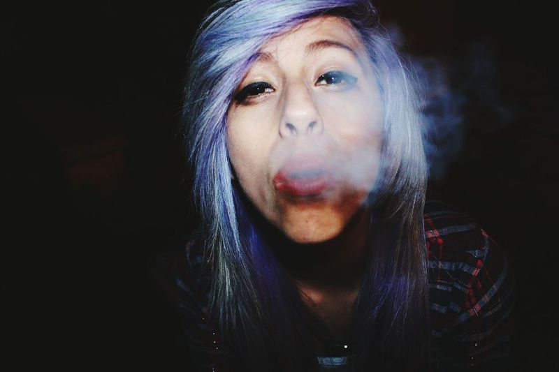 Close-up portrait of young woman blowing smoke