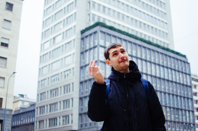 Young man gesturing against buildings in city