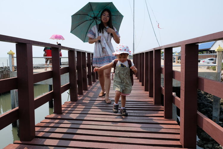 Full length of mother and daughter walking on pier against sky
