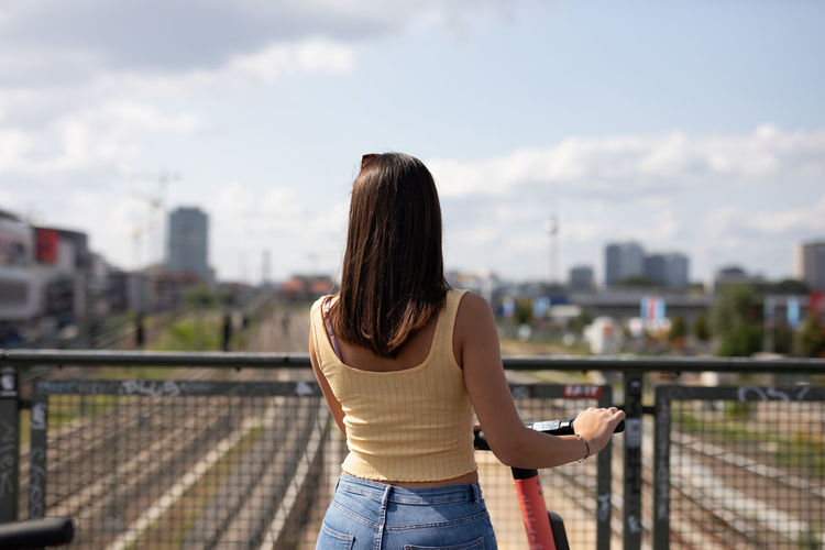 Rear view of woman standing by railing against sky