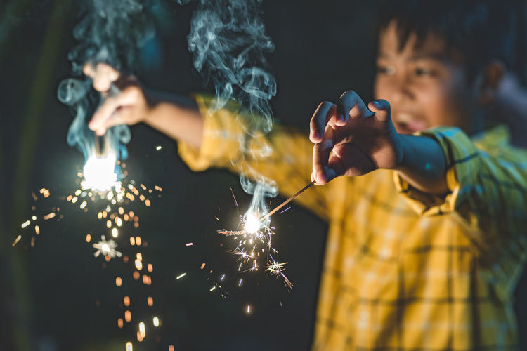 Cheerful boy holding sparklers at night