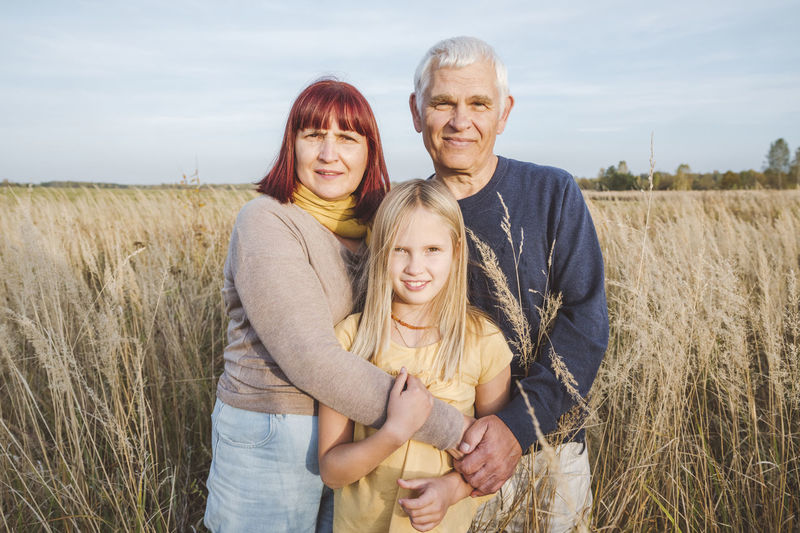 Happy grandparents embracing granddaughter standing at field