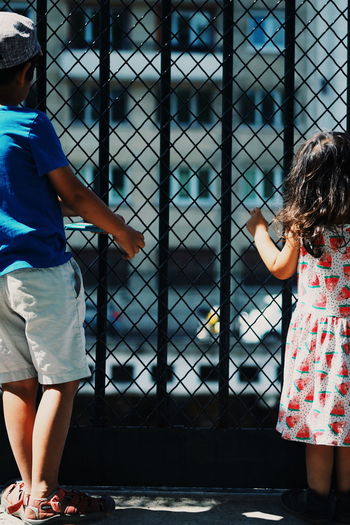 Two children looking out through fenced gate