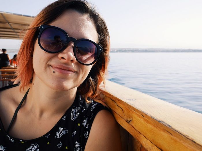 Portrait of smiling young woman in sunglasses against sea