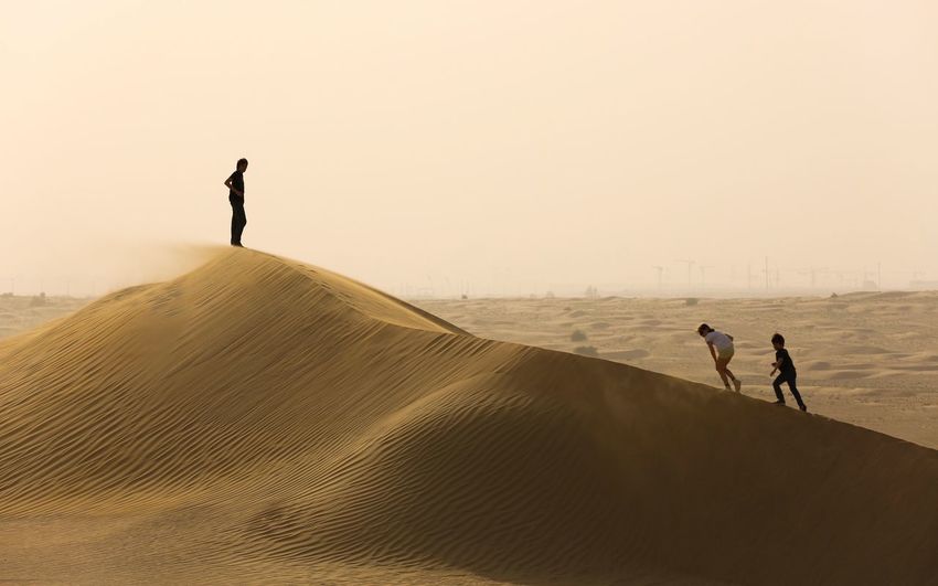 People walking on sand dune against sky