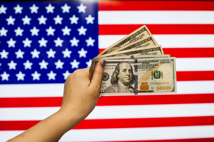 Close-up of hand holding paper currency against american flag
