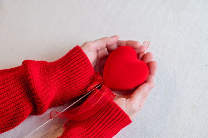 Hands in a red sweater holding a red heart with ribbons. valentine's day holiday person