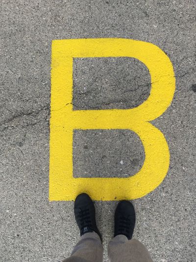 Low section of person standing by yellow letter b on footpath