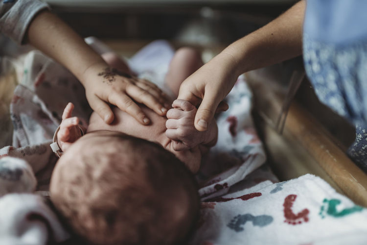 Detail of siblings holding newborn baby brother's hand in hospital