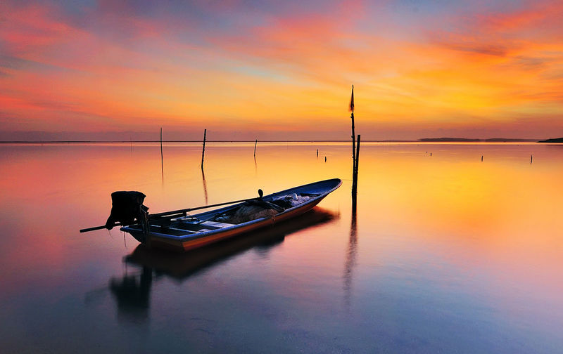 Silhouette boat moored on sea against sky during sunset