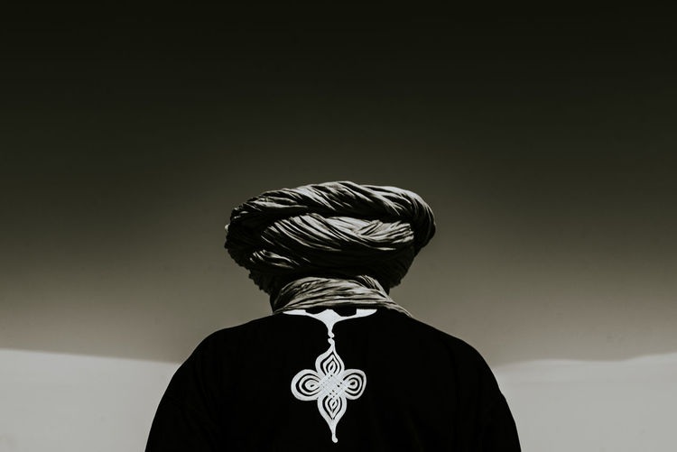Rear view of man in turban standing in desert against clear sky