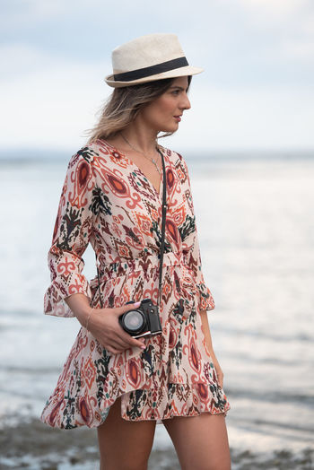 Fashionable caucasian woman holding camera and photographing scenery at the beach. 