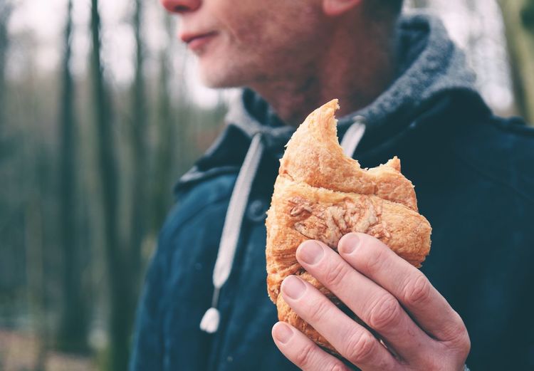 Midsection of man holding croissant in forest