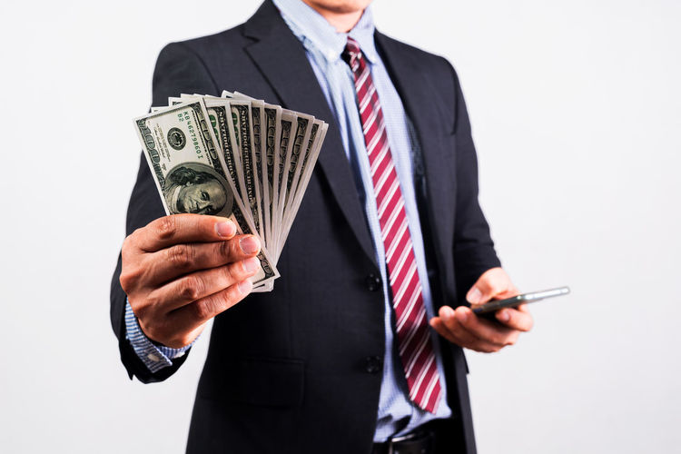 Midsection of businessman holding paper currency against white background