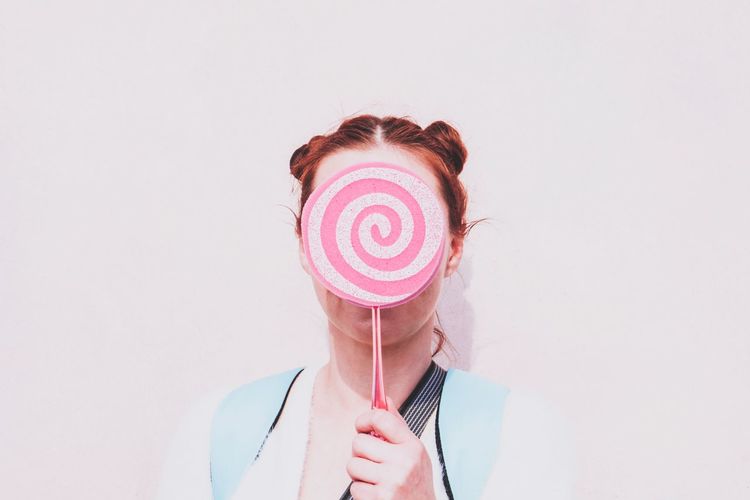 Close-up of woman holding candy against white background