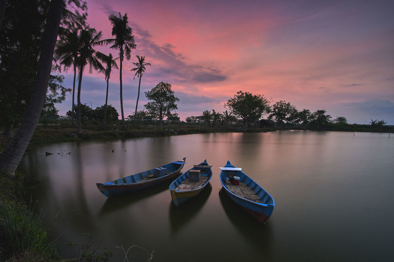 Three empty wooden boats for fishing on a calm water lake at sunset
