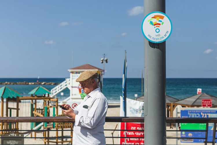 Senior man using smart phone while standing by railing against sea