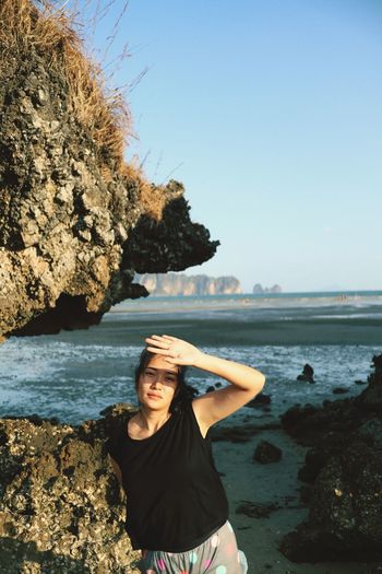Woman standing on rock at beach against clear sky