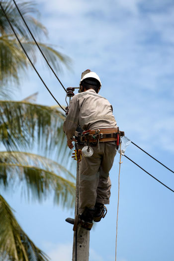 Low angle view of man working on rope against sky